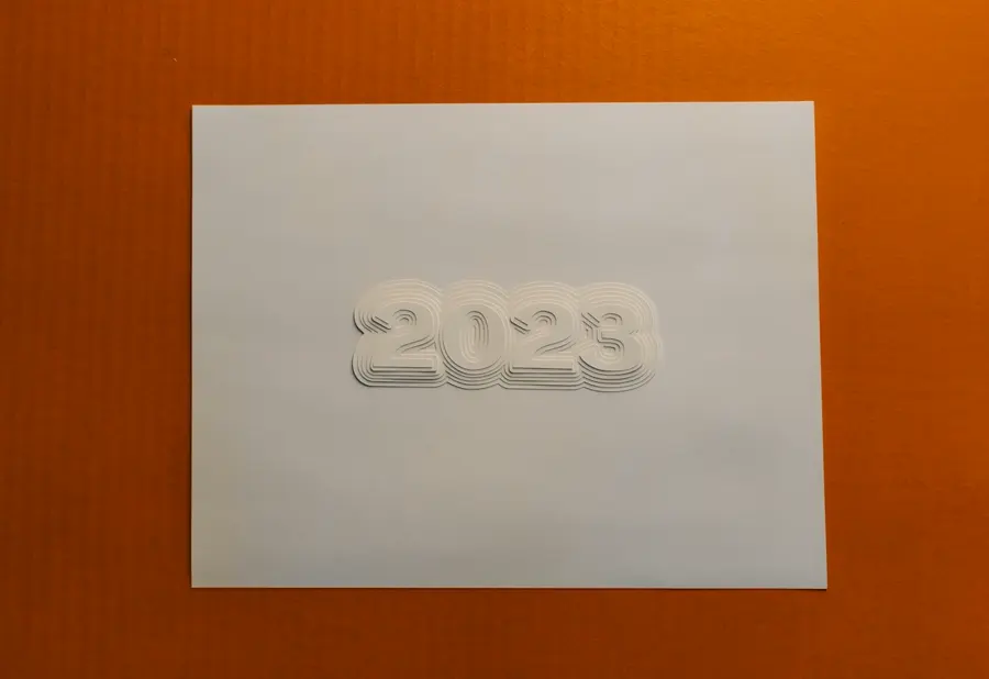 A white sheet of paper blind-embossed with the number 2023 in layered outline letters, on an orange background.