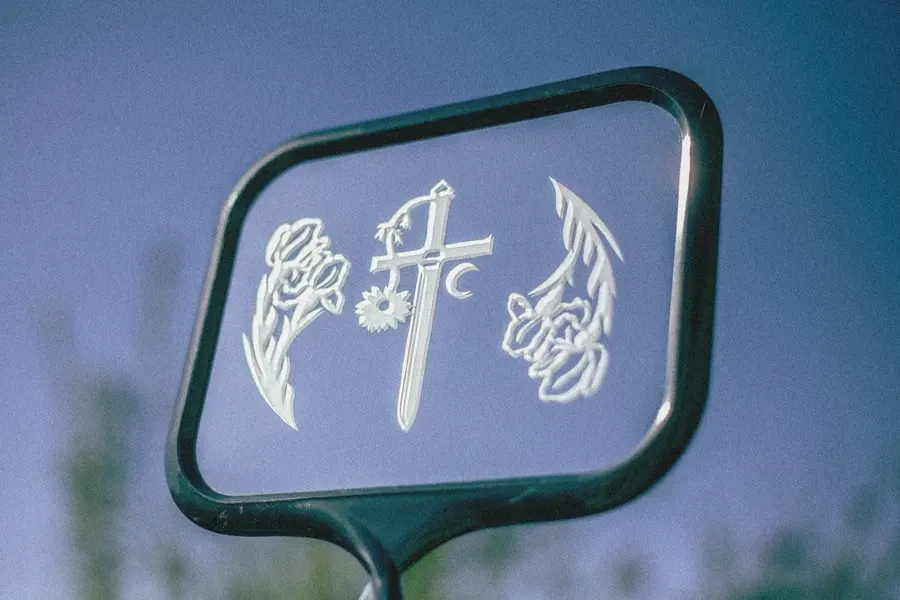 A clear panel in a dark frame with frosted engraved flowers, a sword and a crescent moon against a blue sky.