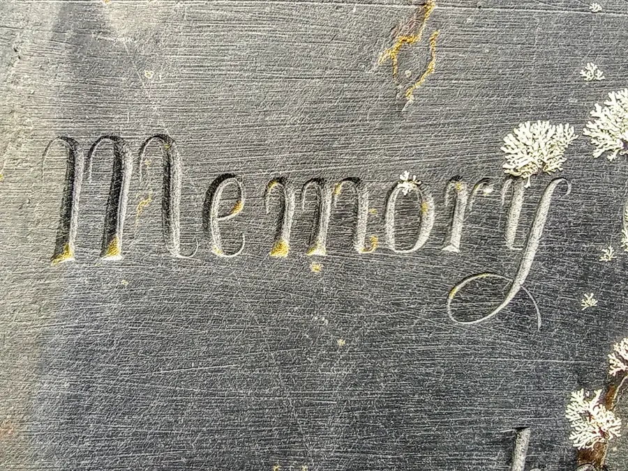 The word memory engraved in flowing script into a dark slate surface with patches of lichen.