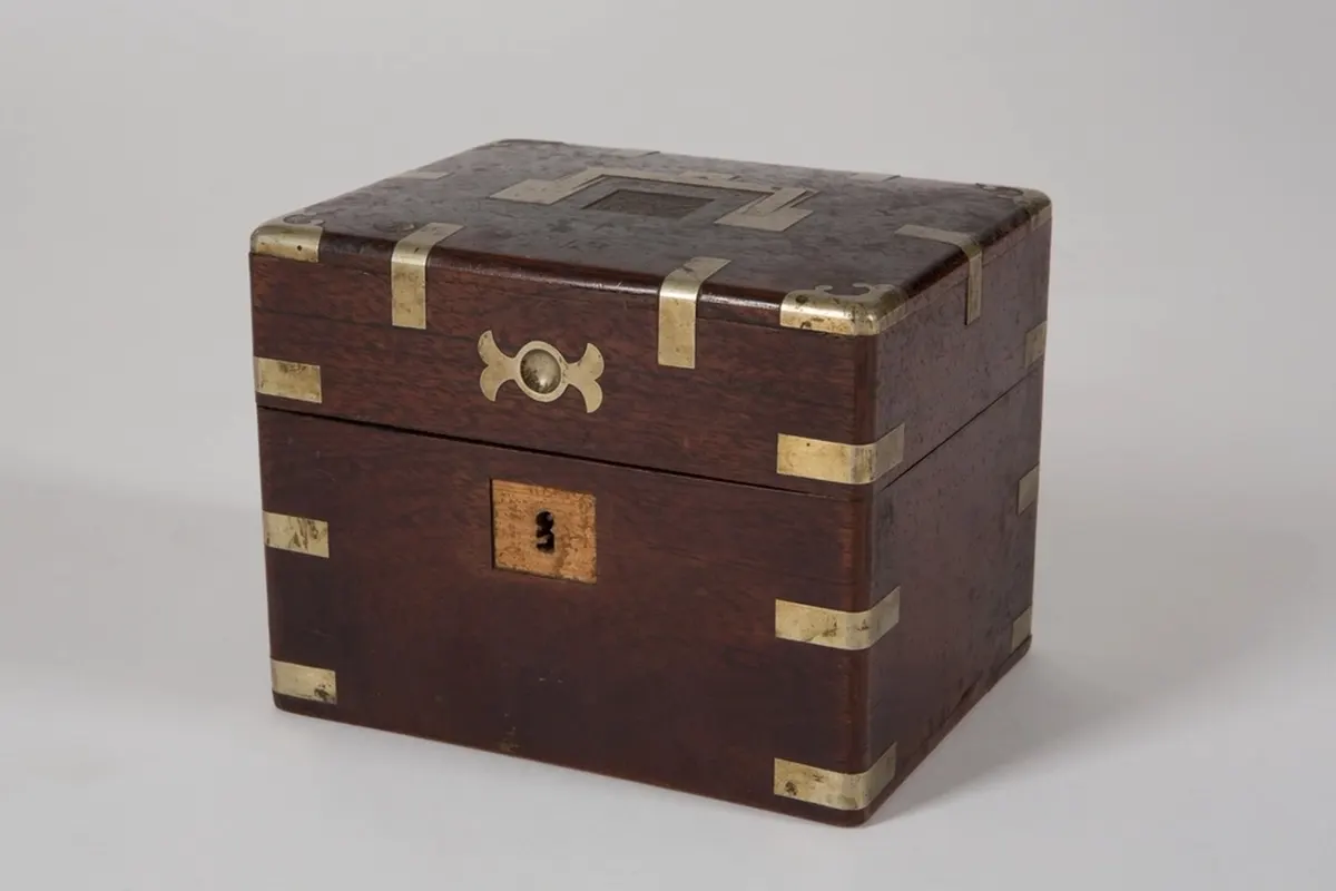 A dark mahogany keepsake box with brass corner fittings, a brass escutcheon and a keyhole plate, on a plain grey backdrop.
