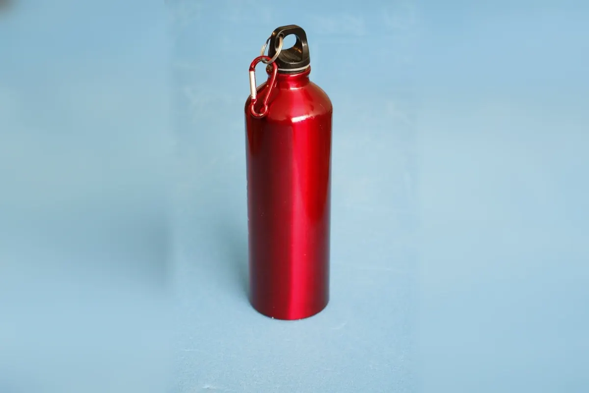 A glossy red aluminium sports bottle with a black screw cap and a red carabiner on a blue backdrop.
