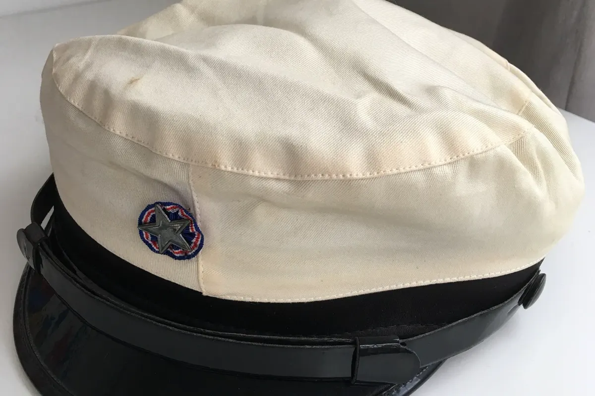 A cream student graduation cap with a black band, glossy black visor and a small star badge, on a white surface.