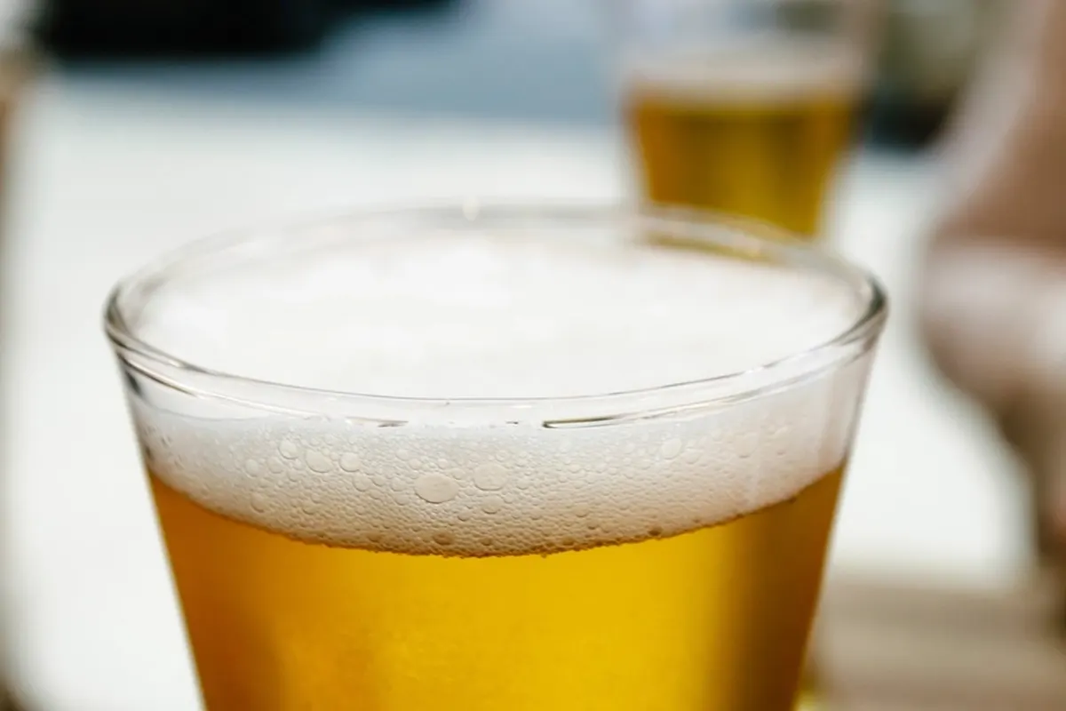 Close view of a clear pint glass of golden beer with a thick white head.