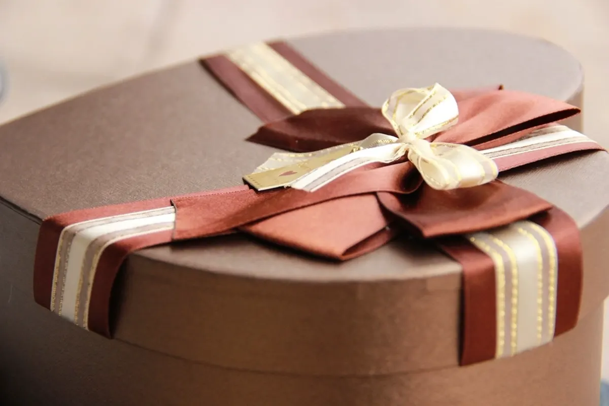 A cocoa-brown heart-shaped gift box tied with a maroon and cream striped satin ribbon and bow.